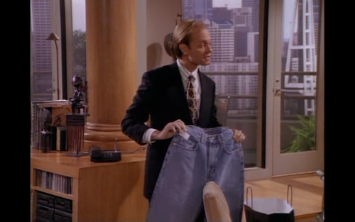 David Hyde Pierce as Niles Crane holds up a pair of blue jeans. 